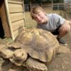 Boy smiling next to a large tortoise.