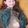 Girl smiling while holding a sloth indoors.
